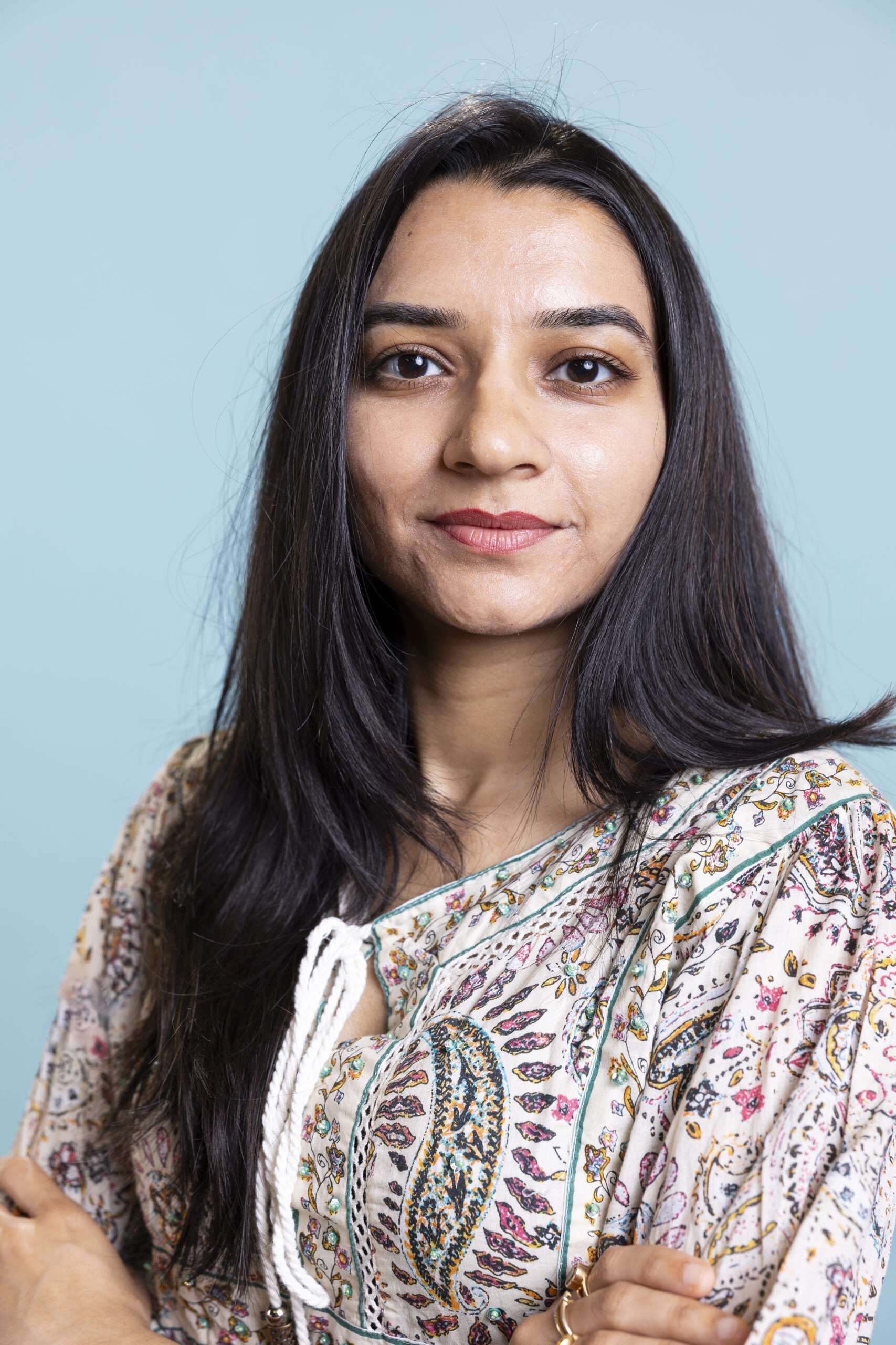 Indian woman posing in a cute stylish outfit on camera and smiling, standing against blue background. Young lively person showing confidence during a photoshoot in the studio.